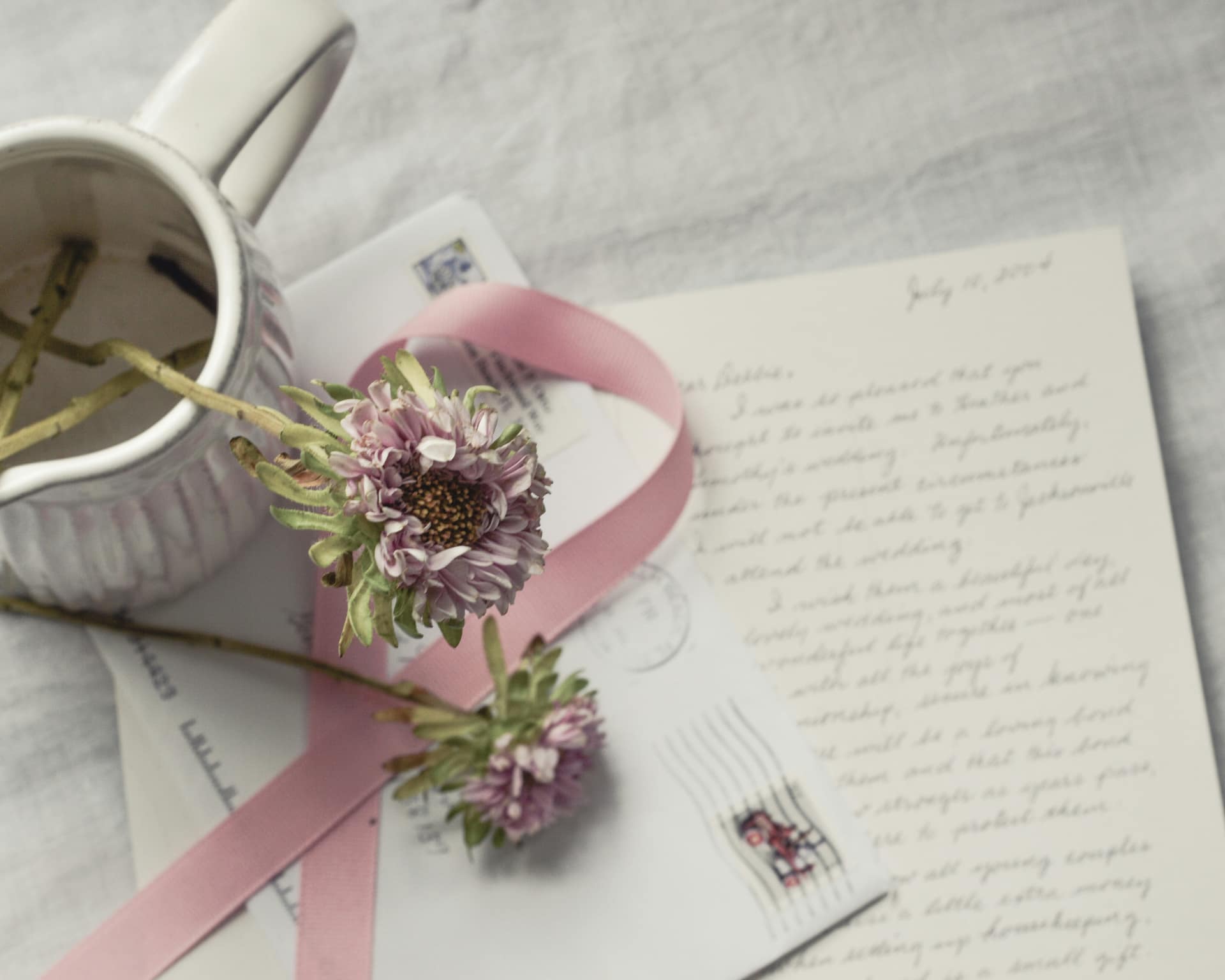 A handwritten letter, a flower and a ribbon on a desk